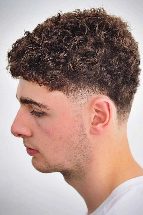 Стрижка с небрежными кудрями сверху и низким конусным фейдом