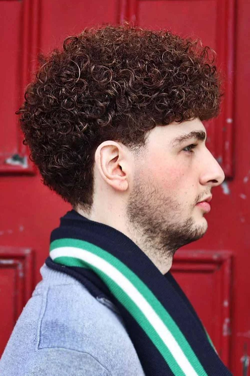 Стрижка с небрежными кудрями сверху и низким конусным фейдом